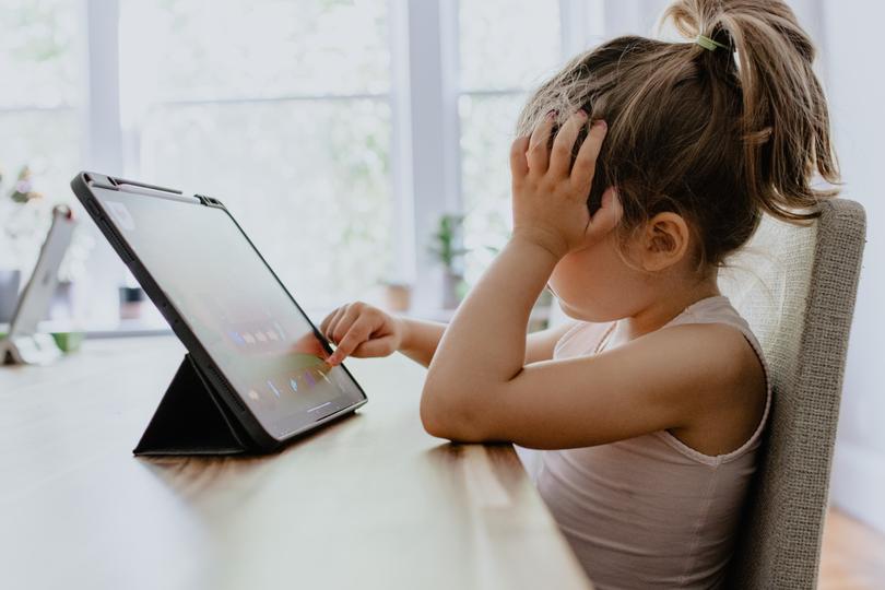 Junges, blondes Mädchen sitzt an einem Tisch und tippt auf dem Tablet. Foto: unsplash | Kelly Sikkema